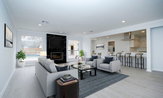 living area with light wood-style floors, a high end fireplace, visible vents, and ornamental molding