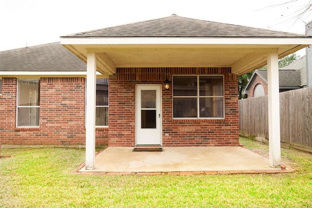 property entrance with brick siding, roof with shingles, and a patio area