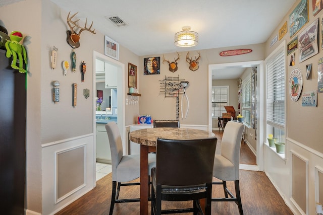 dining area with a wainscoted wall, dark wood-style flooring, and visible vents