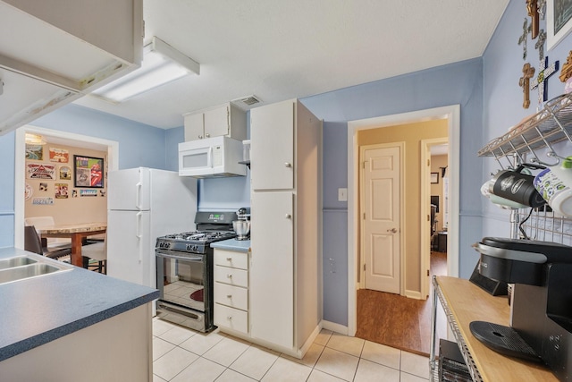 kitchen with white appliances, light tile patterned floors, visible vents, white cabinets, and a sink