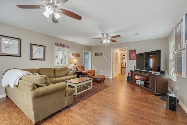 living room featuring a ceiling fan, visible vents, baseboards, and wood finished floors