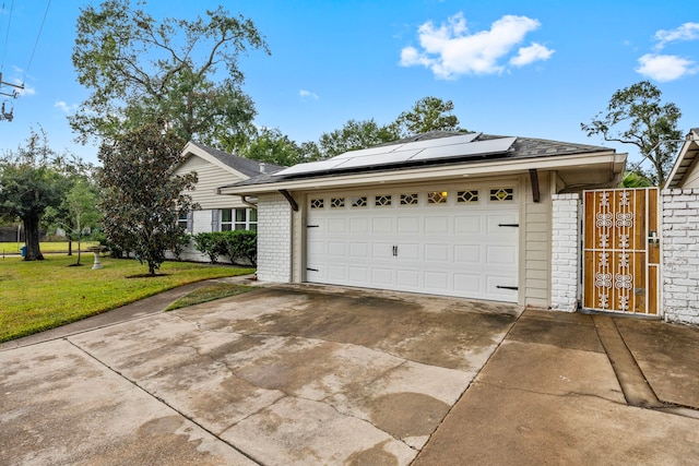 exterior space featuring an attached garage, solar panels, brick siding, concrete driveway, and a front yard