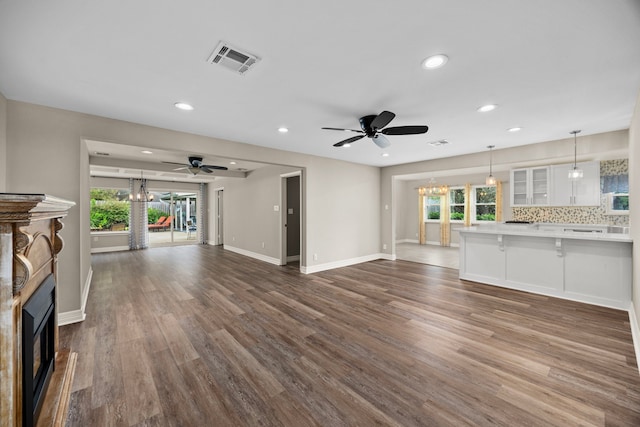 unfurnished living room featuring ceiling fan with notable chandelier, a fireplace, visible vents, baseboards, and dark wood finished floors