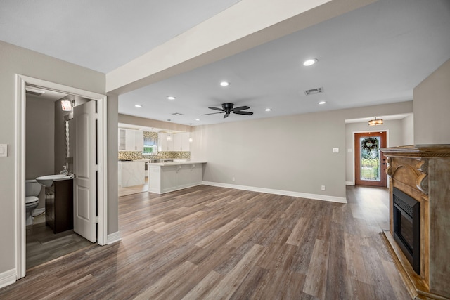 unfurnished living room with baseboards, visible vents, a glass covered fireplace, ceiling fan, and wood finished floors