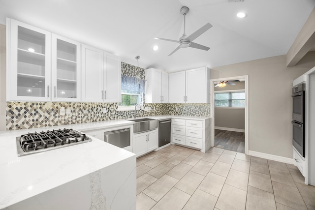 kitchen featuring glass insert cabinets, light stone counters, stainless steel appliances, white cabinetry, and a sink