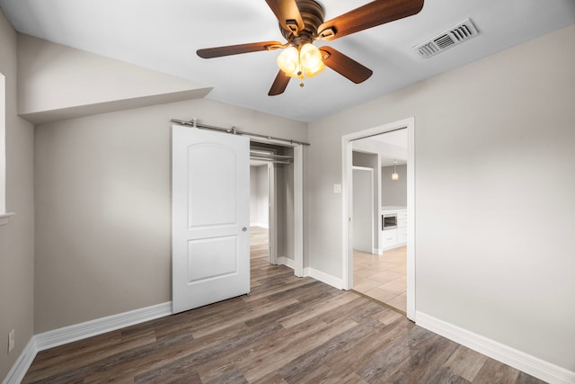 unfurnished bedroom with a barn door, wood finished floors, visible vents, and baseboards