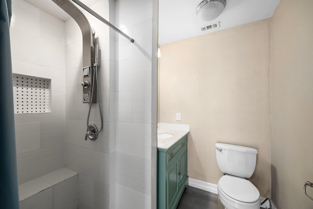 bathroom with baseboards, visible vents, toilet, a tile shower, and vanity