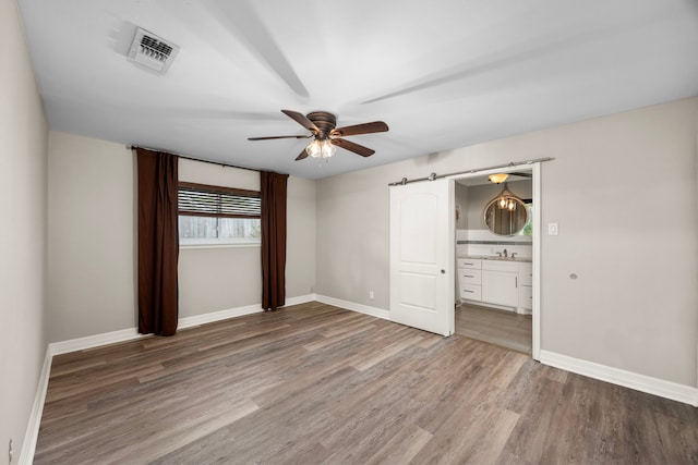 unfurnished bedroom with visible vents, a barn door, a sink, wood finished floors, and baseboards