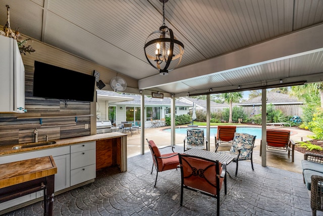 view of patio / terrace with an outdoor kitchen, a ceiling fan, a sink, fence, and an outdoor pool