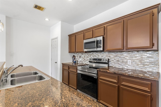 kitchen with visible vents, dark countertops, a sink, stainless steel appliances, and backsplash