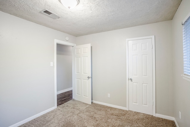 unfurnished bedroom with baseboards, visible vents, a textured ceiling, and light colored carpet