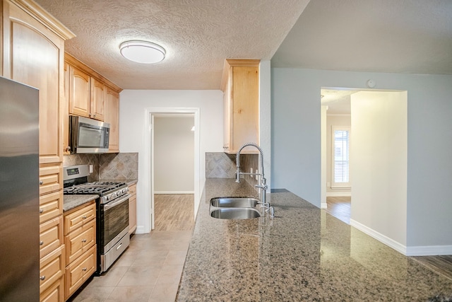 kitchen featuring light brown cabinets, stainless steel appliances, a sink, and light stone countertops