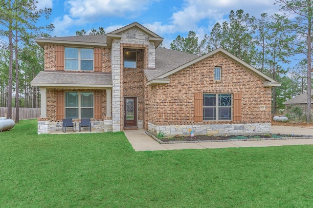 view of front facade with roof with shingles, brick siding, a front yard, fence, and stone siding