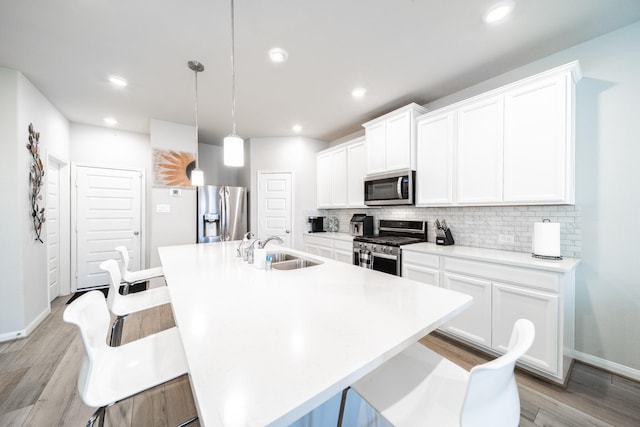 kitchen with an island with sink, appliances with stainless steel finishes, hanging light fixtures, light countertops, and a sink