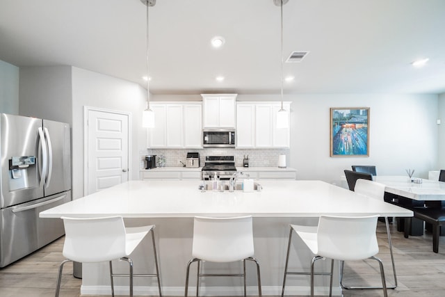 kitchen featuring visible vents, hanging light fixtures, appliances with stainless steel finishes, light countertops, and a center island with sink