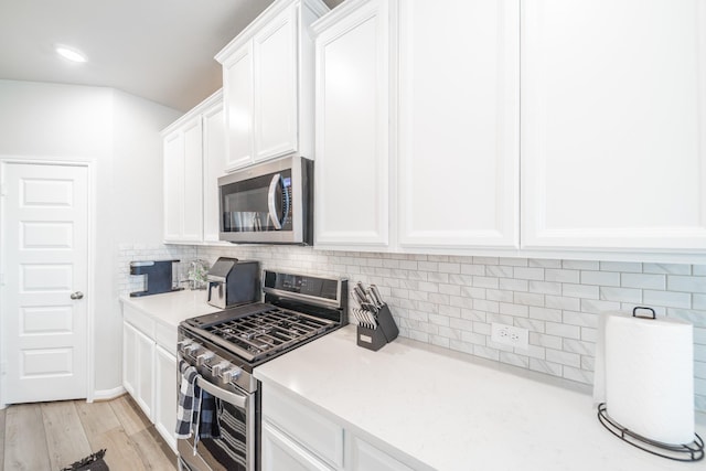 kitchen featuring light wood-style flooring, white cabinetry, light countertops, appliances with stainless steel finishes, and decorative backsplash