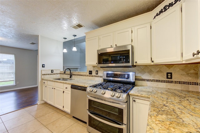 kitchen featuring decorative light fixtures, light tile patterned floors, stainless steel appliances, visible vents, and a sink