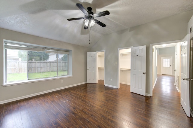 unfurnished bedroom with dark wood-style floors, multiple windows, a walk in closet, and baseboards