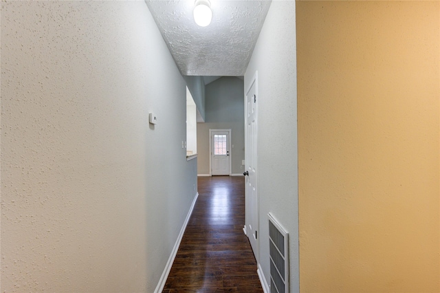 hall with a textured ceiling, a textured wall, dark wood-type flooring, visible vents, and baseboards