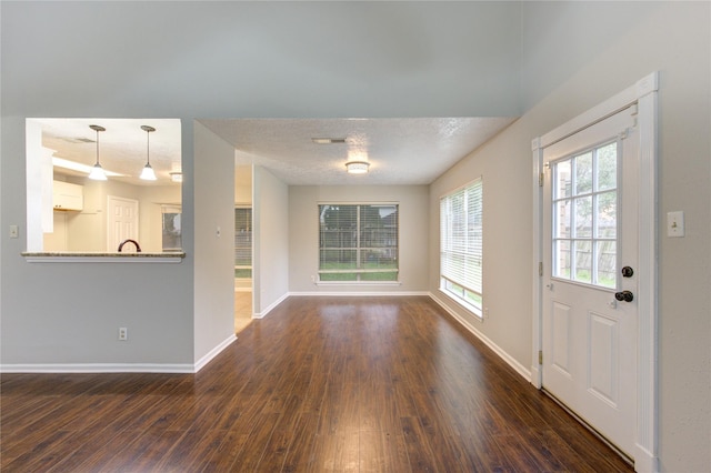 interior space with a textured ceiling, dark wood-type flooring, visible vents, and baseboards