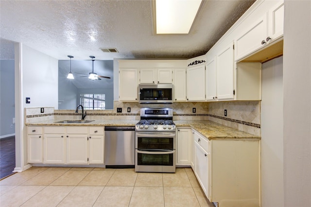 kitchen featuring appliances with stainless steel finishes, white cabinets, a sink, and decorative light fixtures