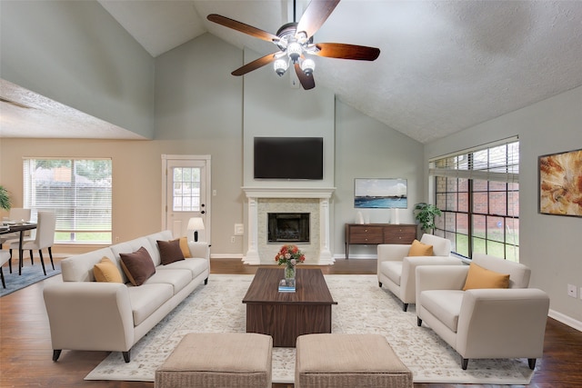 living area with high vaulted ceiling, a fireplace, wood finished floors, a ceiling fan, and baseboards