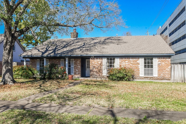 ranch-style house featuring a shingled roof, brick siding, a chimney, and a front lawn