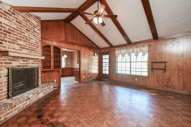 unfurnished living room with ceiling fan, high vaulted ceiling, wooden walls, a fireplace, and beamed ceiling