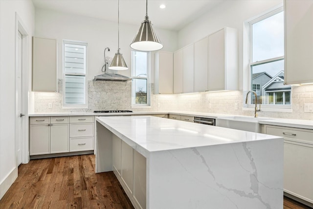 kitchen with decorative light fixtures, a wealth of natural light, white cabinetry, a kitchen island, and light stone countertops