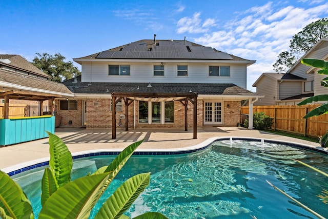 rear view of property with fence private yard, french doors, a patio area, roof mounted solar panels, and brick siding