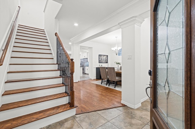 entrance foyer with light tile patterned floors, crown molding, stairway, decorative columns, and an inviting chandelier