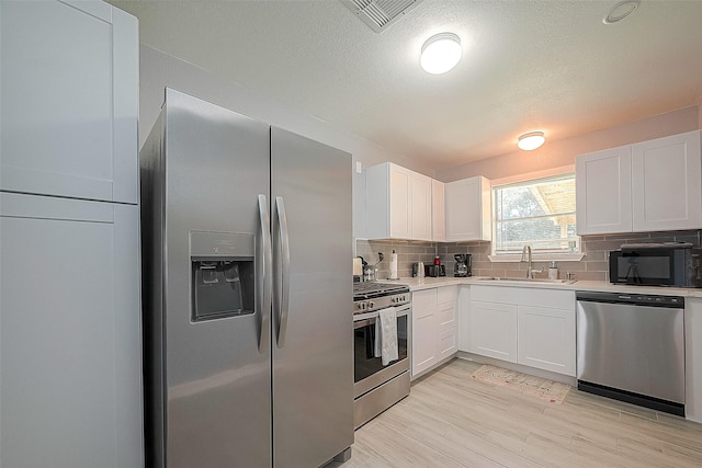 kitchen with appliances with stainless steel finishes, white cabinets, light countertops, and a sink