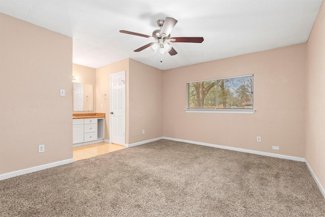 unfurnished bedroom featuring light colored carpet, connected bathroom, baseboards, and ceiling fan