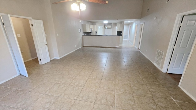 unfurnished living room with a ceiling fan, baseboards, visible vents, and a high ceiling