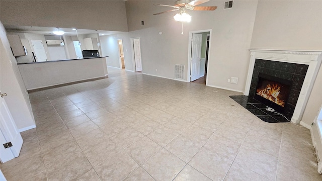 unfurnished living room featuring ceiling fan, a tile fireplace, visible vents, and baseboards