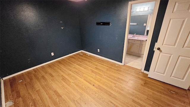 unfurnished bedroom featuring ensuite bathroom, light wood-type flooring, a sink, and baseboards