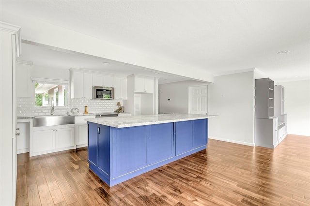 kitchen with stainless steel microwave, a center island, light stone countertops, white cabinetry, and a sink