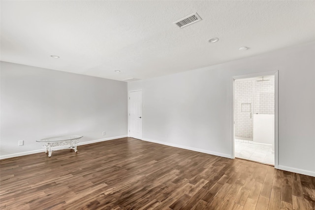 unfurnished room featuring baseboards, visible vents, dark wood finished floors, and a textured ceiling