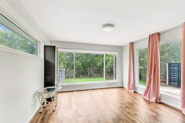 unfurnished living room featuring a wealth of natural light, a textured ceiling, baseboards, and wood finished floors