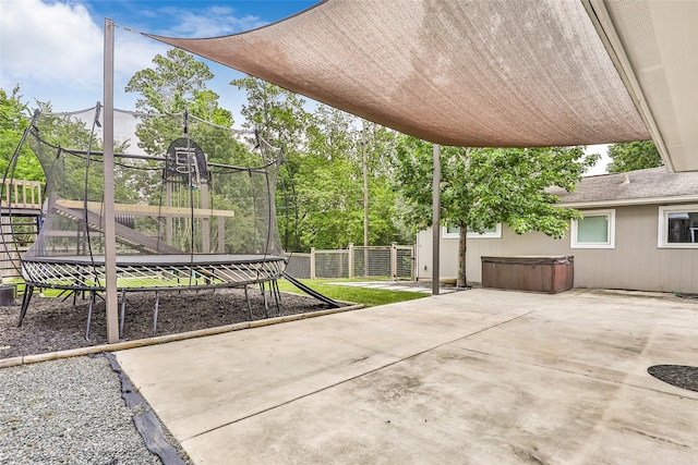 view of patio featuring a trampoline, a fenced backyard, and a hot tub