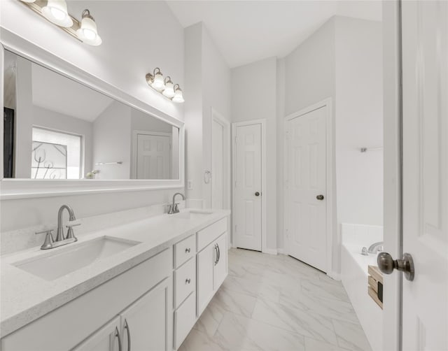 bathroom with double vanity, marble finish floor, a garden tub, and a sink