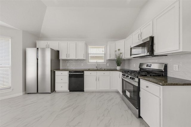 kitchen featuring stainless steel appliances, a sink, white cabinets, vaulted ceiling, and dark stone counters