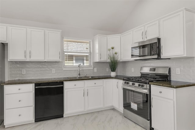 kitchen with lofted ceiling, appliances with stainless steel finishes, white cabinetry, a sink, and dark stone countertops