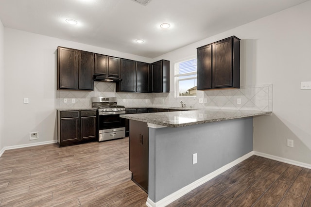 kitchen featuring light wood-style floors, gas stove, dark brown cabinetry, a peninsula, and under cabinet range hood