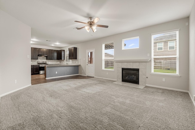 unfurnished living room with ceiling fan, light carpet, a fireplace, a sink, and baseboards