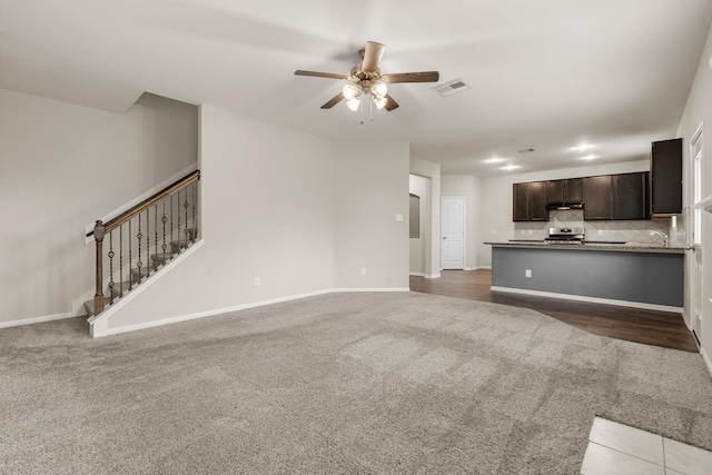 unfurnished living room featuring baseboards, visible vents, a ceiling fan, stairs, and carpet floors