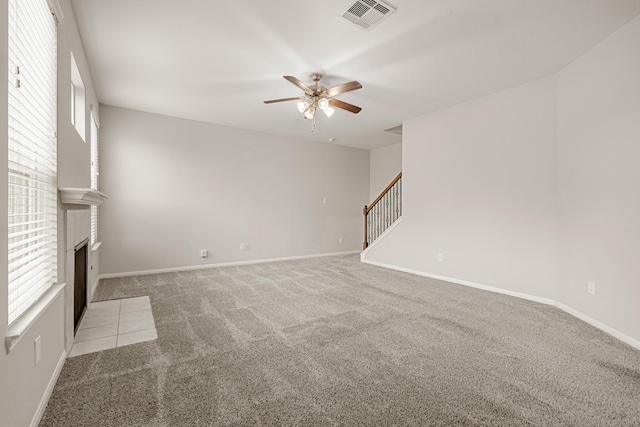 unfurnished living room featuring visible vents, stairway, a fireplace with flush hearth, a ceiling fan, and light carpet