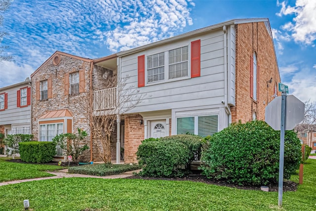 view of property featuring a balcony, a front lawn, and brick siding