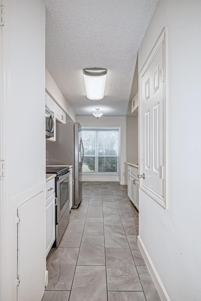 kitchen with appliances with stainless steel finishes, light countertops, white cabinets, and a textured ceiling