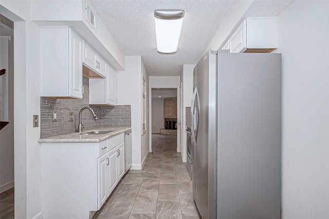 kitchen with a textured ceiling, stainless steel appliances, a sink, white cabinets, and tasteful backsplash